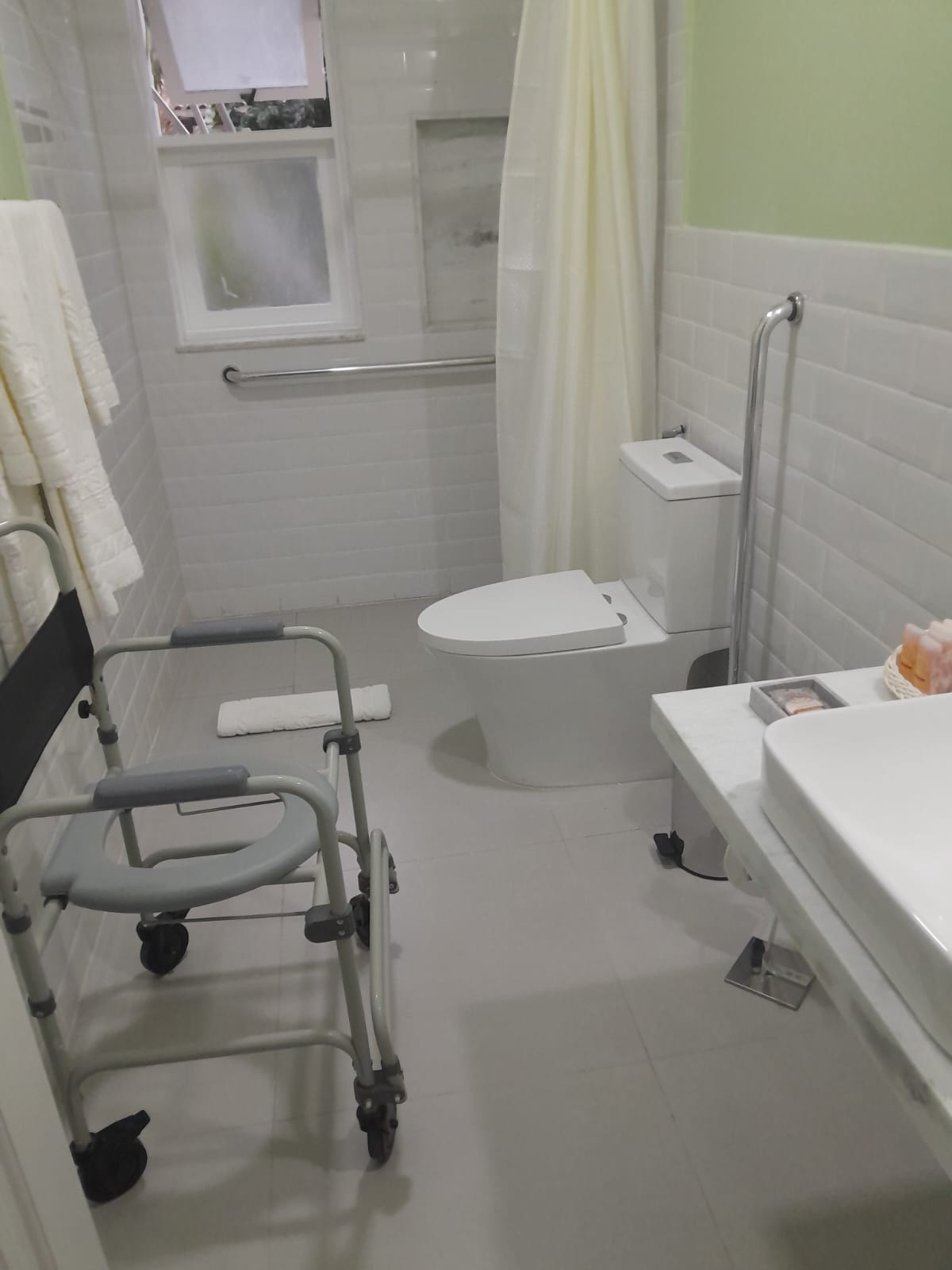 Baño adaptado de la Pousada Corsário Búzios con barras de apoyo, inodoro y silla de ducha con ruedas.