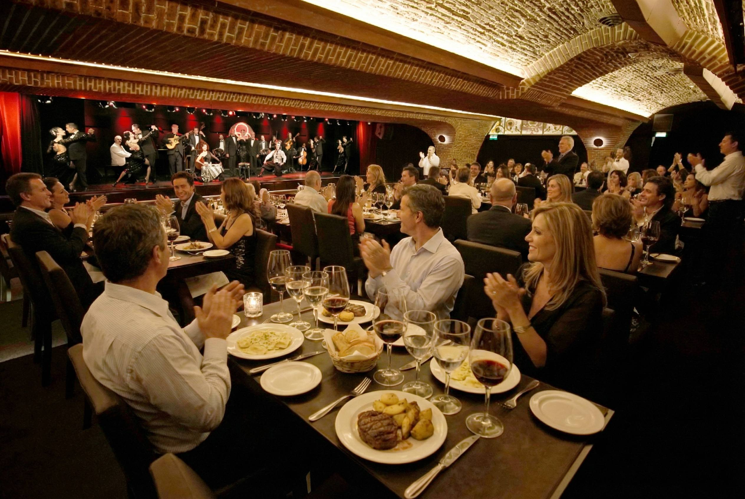 Guests seated at dining tables applauding the show at Michelangelo, beneath a vaulted brick ceiling.