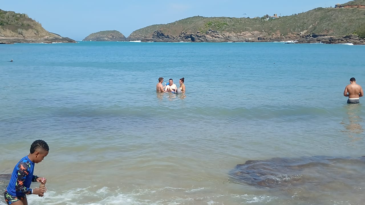 Vista de una playa de Búzios con personas disfrutando del mar y colinas al fondo.
