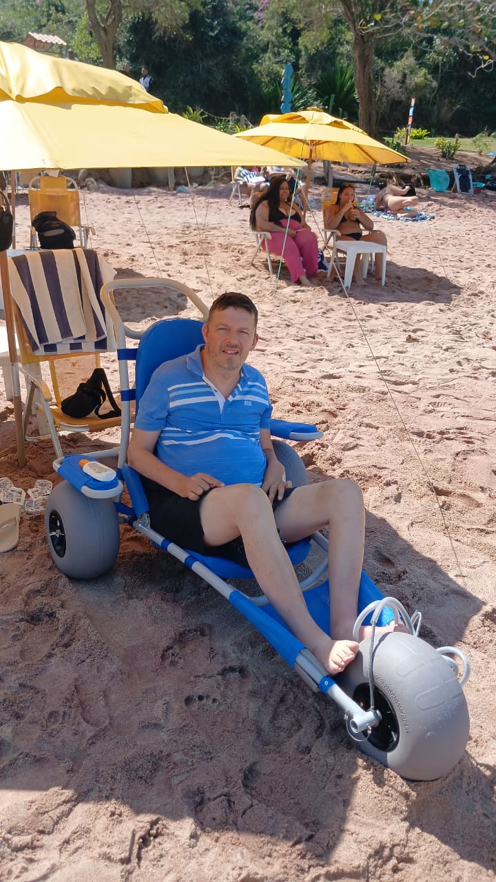 Persona sentada en una silla anfibia azul sobre la arena de una playa de Búzios.